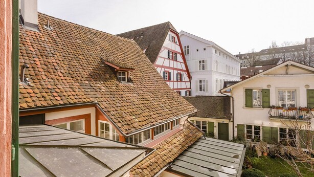 A traditional European town with a mix of residential buildings, including a house with a sloped roof and a white building with a gabled roof.