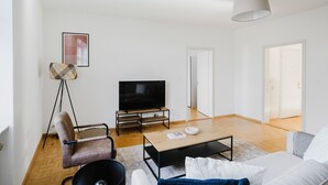 A modern living room with a flat-screen TV, a sofa, a coffee table, and a floor lamp.