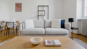 A modern living room with a light grey sofa, a wooden coffee table, and a book titled 'Identity Economics'.