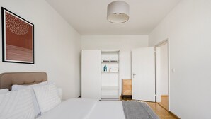 A bedroom with a bed, a wardrobe, a bedside table, and a hanging light fixture.