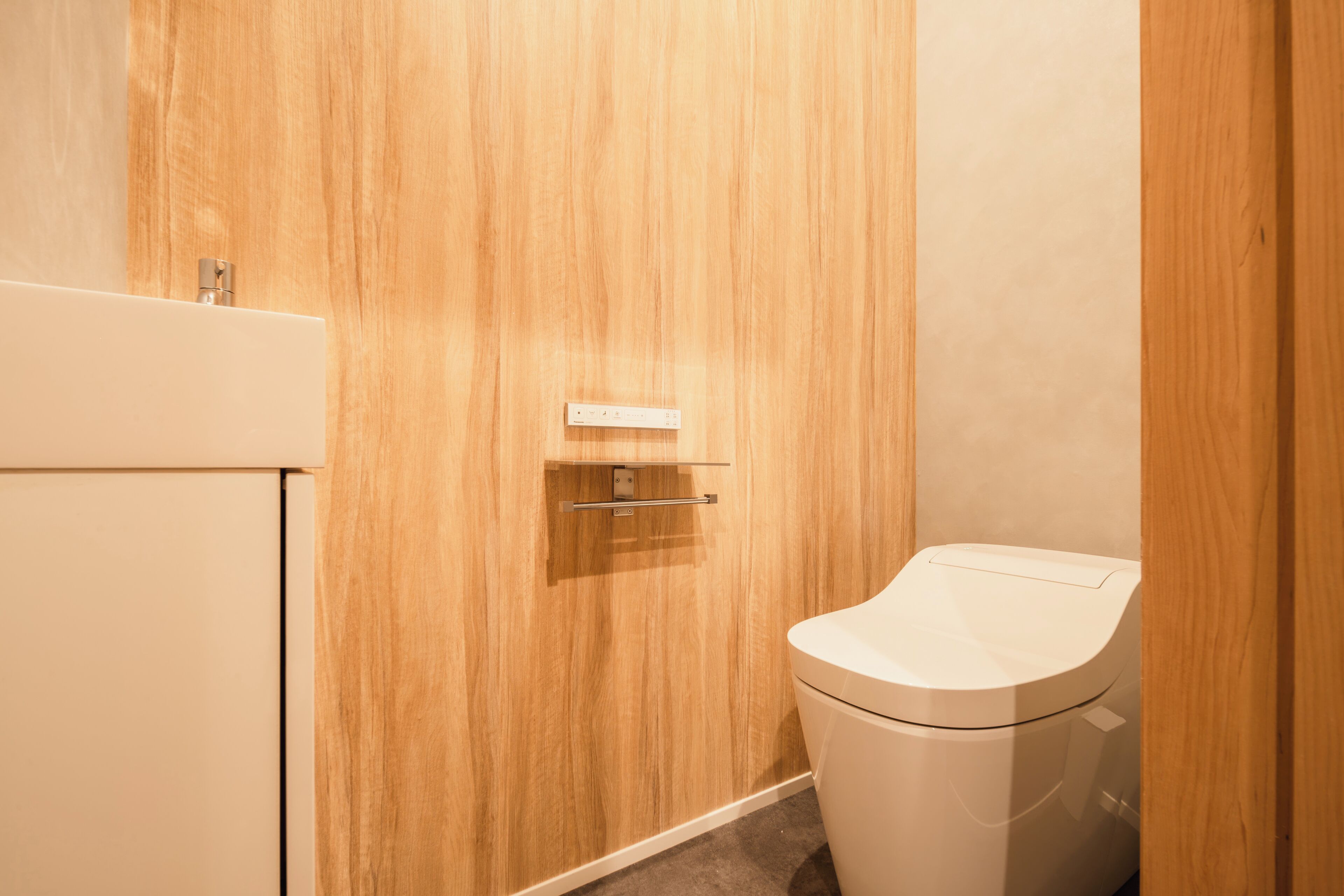 A bathroom with a wooden vanity, a toilet, and a wall-mounted electrical outlet.