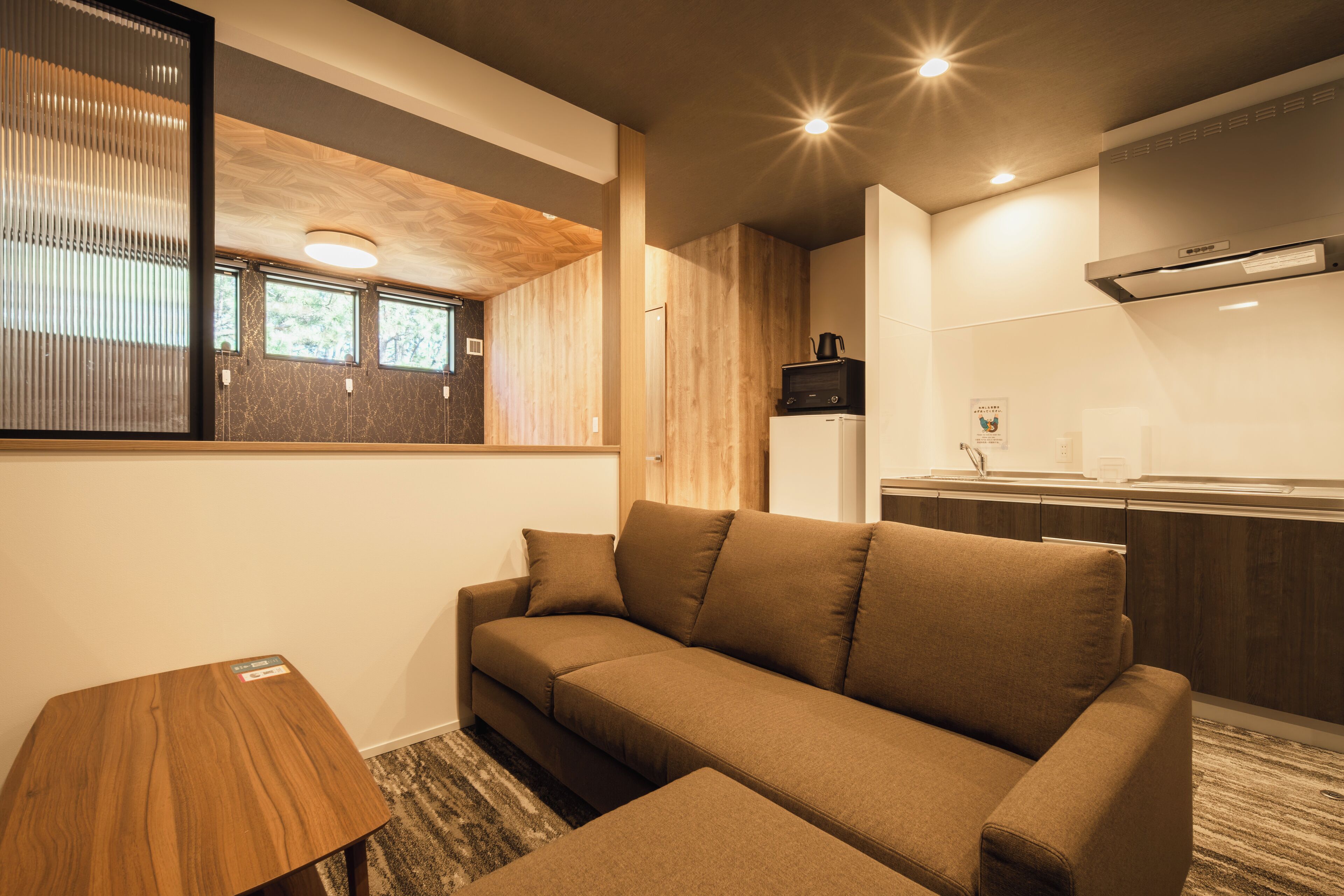 Una sala de estar moderna con un sofá, una mesita de madera y una zona de cocina con microondas y cafetera.