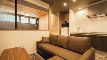A modern living room with a sofa, a small wooden table, and a kitchen area with a microwave and a coffee maker.