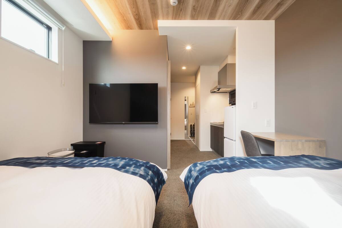 Een hotelkamer met twee bedden, een televisie, een bureau en een kitchenette.
