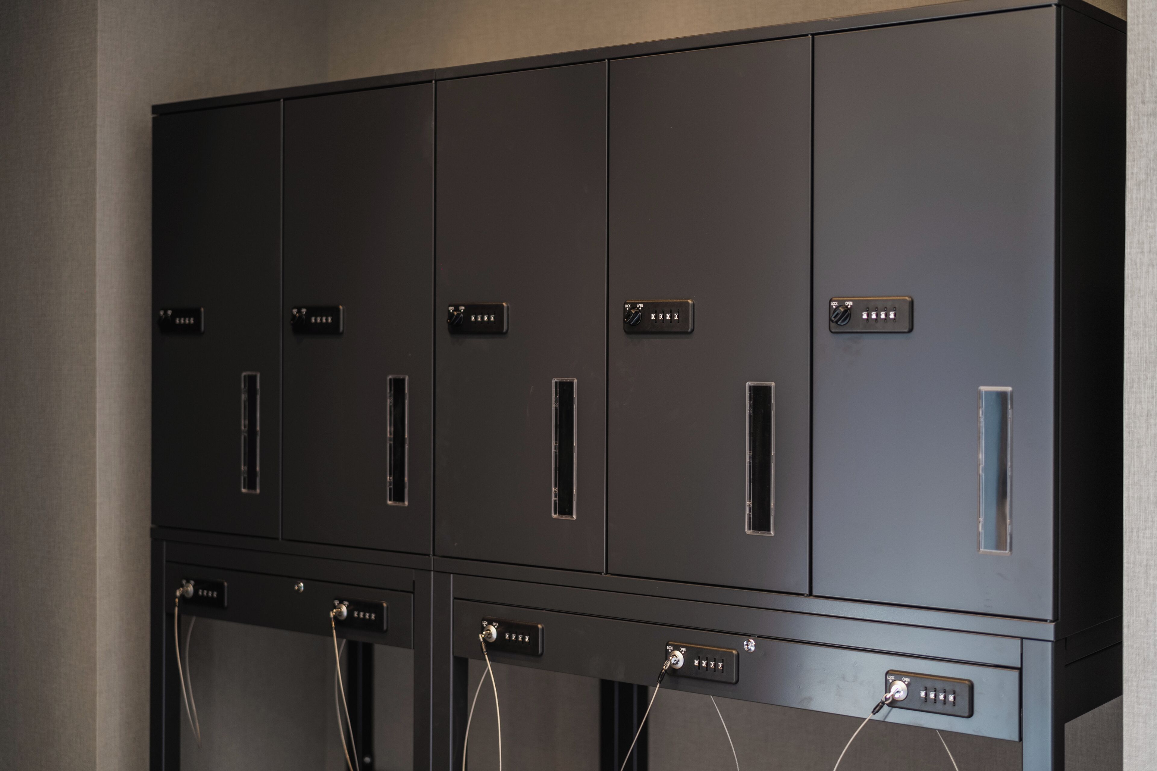 Una hilera de taquillas oscuras de metal con etiquetas y un panel de control debajo.