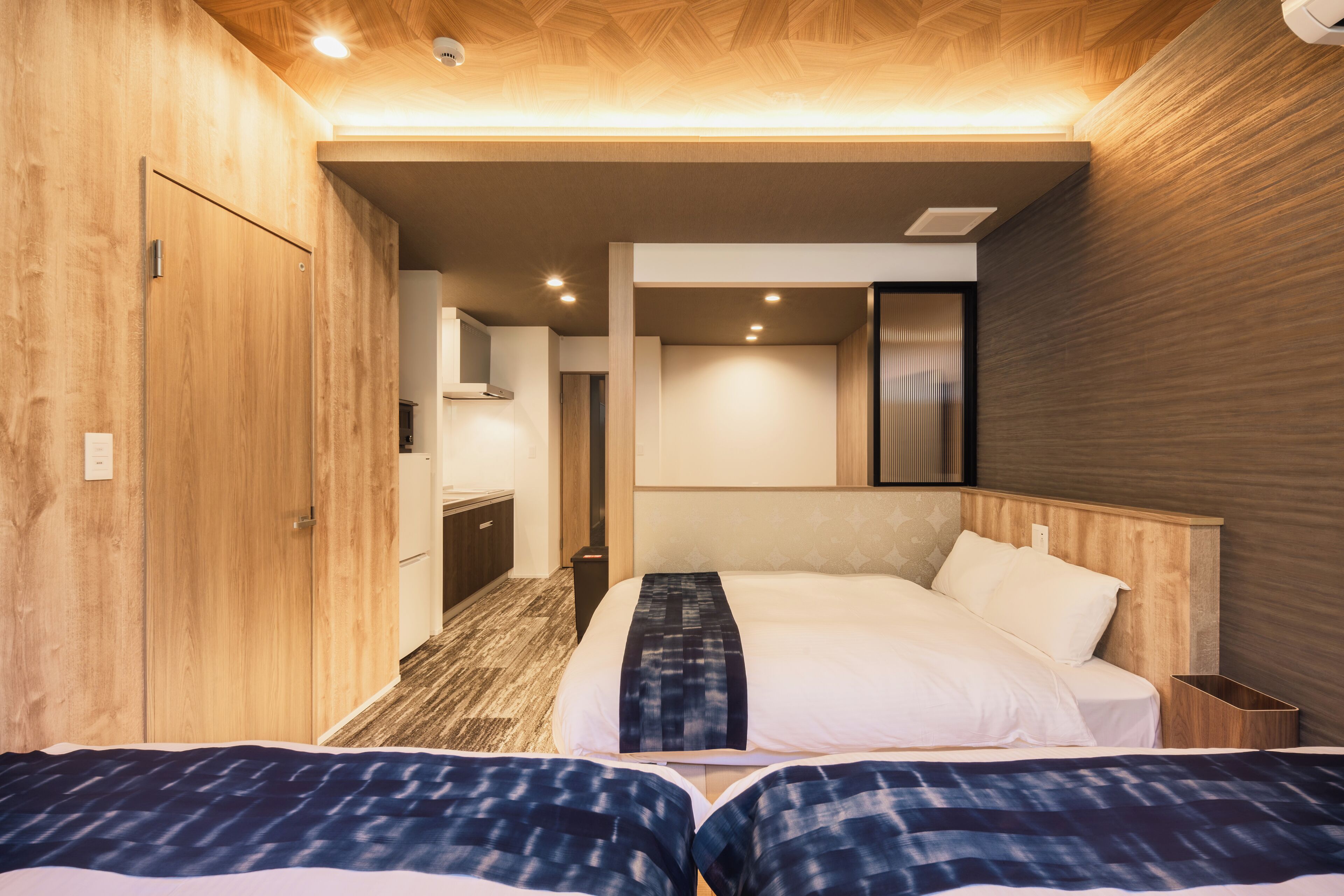 Quarto de hotel com duas camas, paredes de madeira, uma kitchenette pequena e um banheiro.