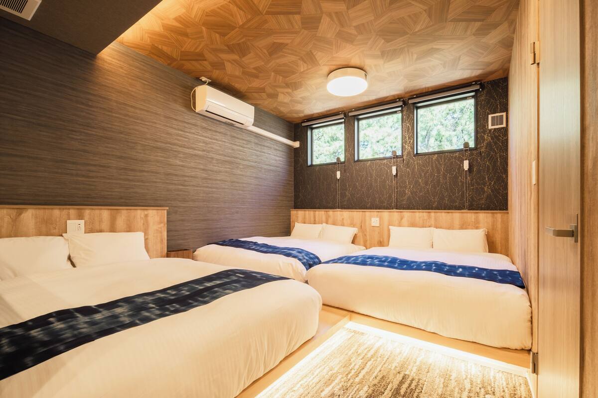 Een hotelkamer met twee bedden, houten hoofdeinden, een groot raam en een plafond met een geometrisch patroon.