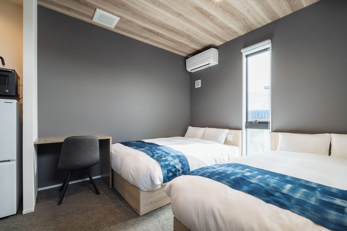Een slaapkamer met twee bedden, een bureau, een stoel en een airconditioning.