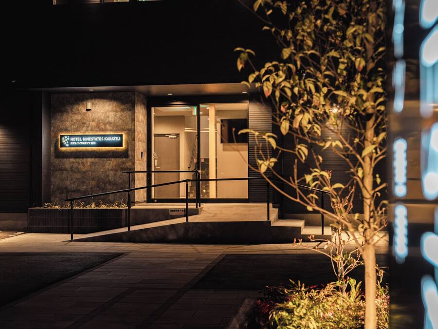 A hotel entrance with a sign, a staircase, and a small tree.