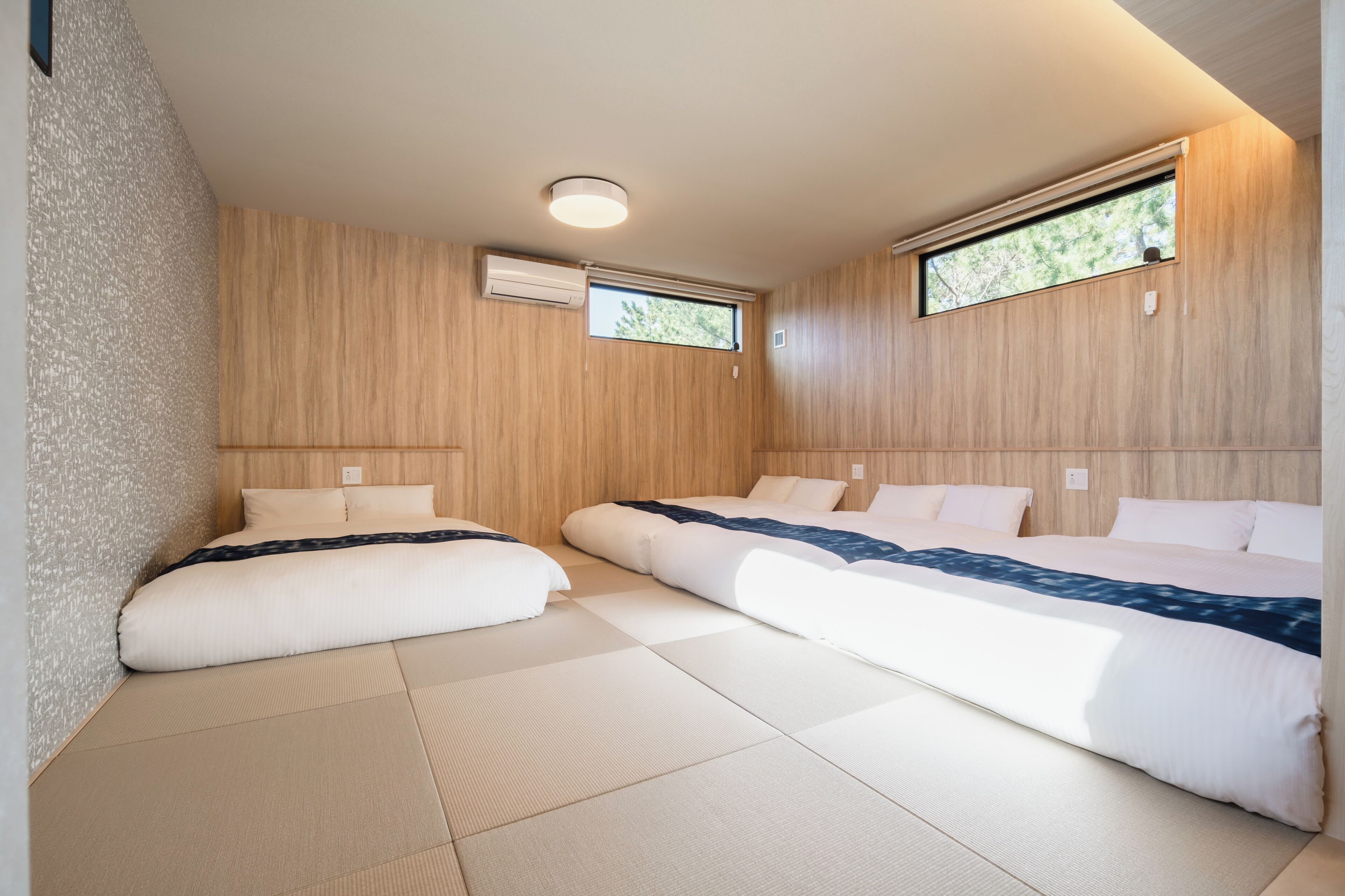 Un dormitorio moderno con dos camas, paneles de madera y ventanas amplias.