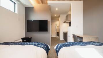 Una habitación de hotel con dos camas, televisión, escritorio y kitchenette.