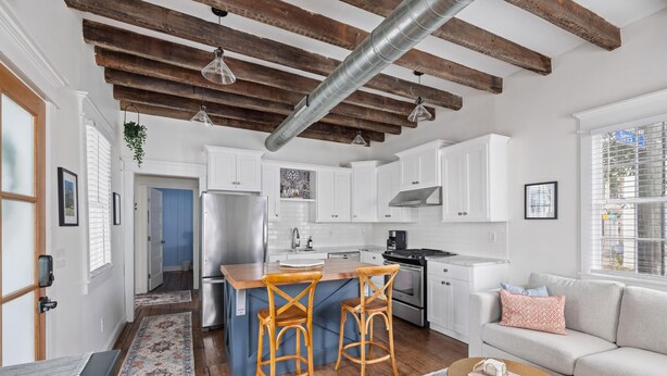 Una cocina moderna con armarios blancos, una isla central con taburetes y un refrigerador de acero inoxidable.