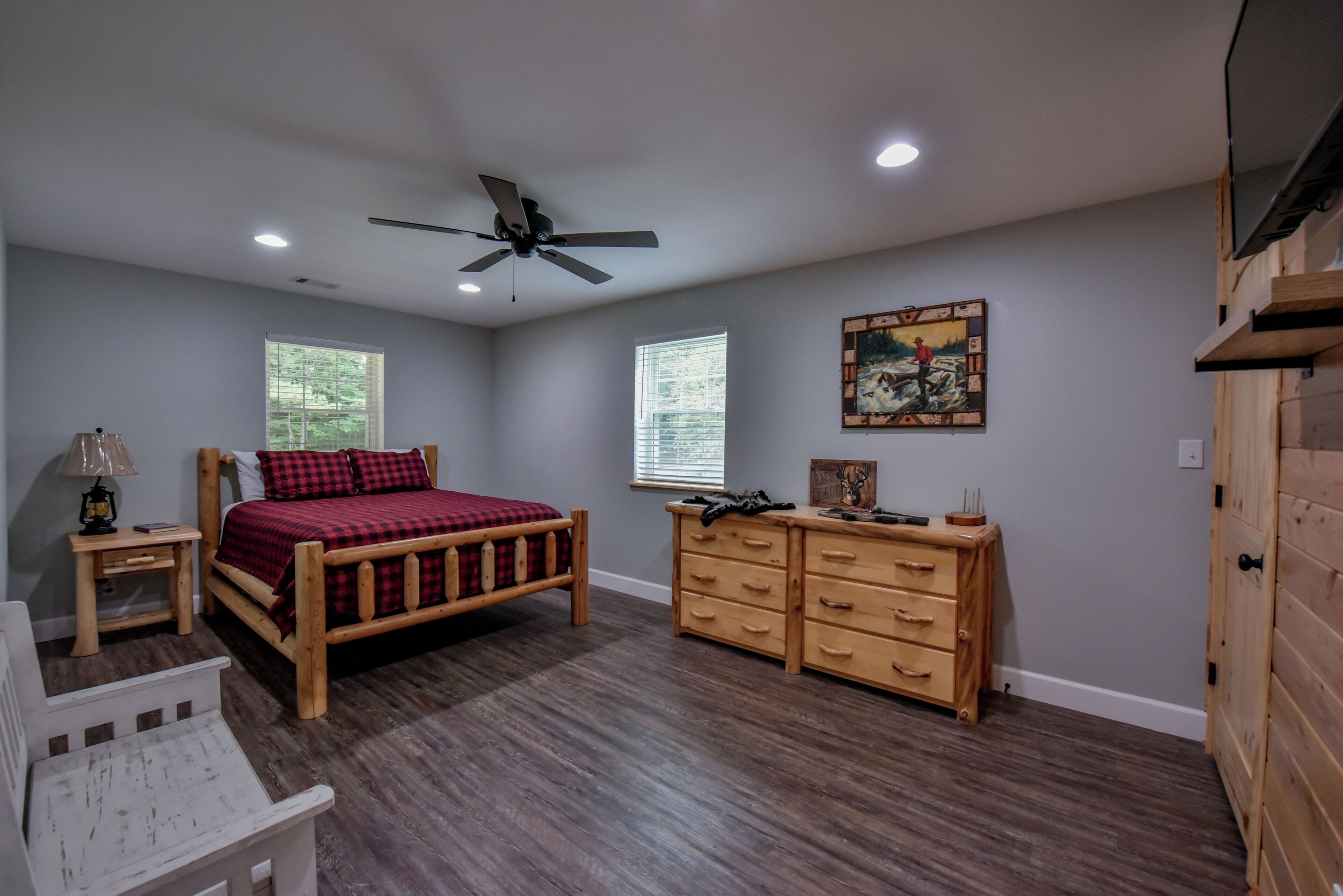 A bedroom with a wooden bed, a dresser, a nightstand, and a ceiling fan.