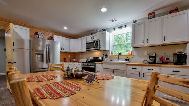 A modern kitchen with white cabinets, stainless steel appliances, and a wooden dining table with red placemats.