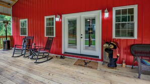 A red exterior with white-framed windows, a wooden deck, rocking chairs, and a welcome mat.