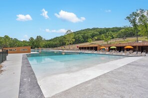 Una piscina con sillas de descanso y sombrillas, rodeada por una terraza de madera y un paisaje montañoso.