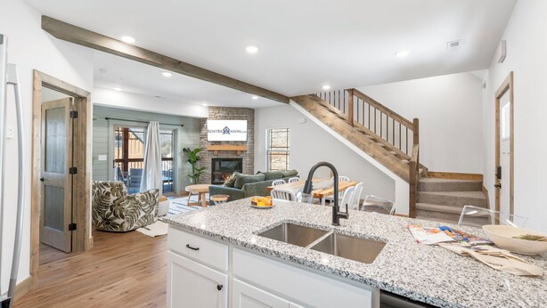 A modern kitchen with granite countertops, a stainless steel sink, and wooden flooring.