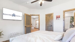 A bedroom with a bed, a ceiling fan, and a TV mounted on the wall displaying a logo.