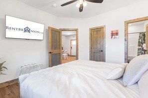 Un dormitorio con una cama, un ventilador de techo y un televisor montado en la pared mostrando un logotipo.