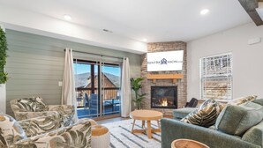 A modern living room with a fireplace, a sofa set, a dining table, and a view of the outside.
