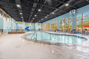 Una piscina interior de diseño curvo, rodeada de sillones de descanso y una pared decorativa de piedra.