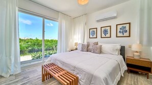 Quarto com uma cama grande, um banco de madeira, uma mesa de cabeceira e um ar condicionado fixado na parede.