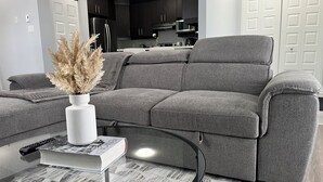 Una sala de estar moderna con un sofá gris, una mesa de centro y un jarrón con plantas secas.