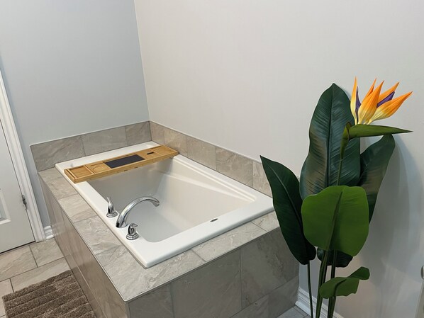 Een badkamer met een wit bad, een houten dienblad en een grote groene plant met oranje bloemen.