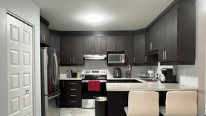 Una cocina moderna con armarios oscuros, electrodomésticos de acero inoxidable, una isla central con taburetes altos y piso de baldosas.