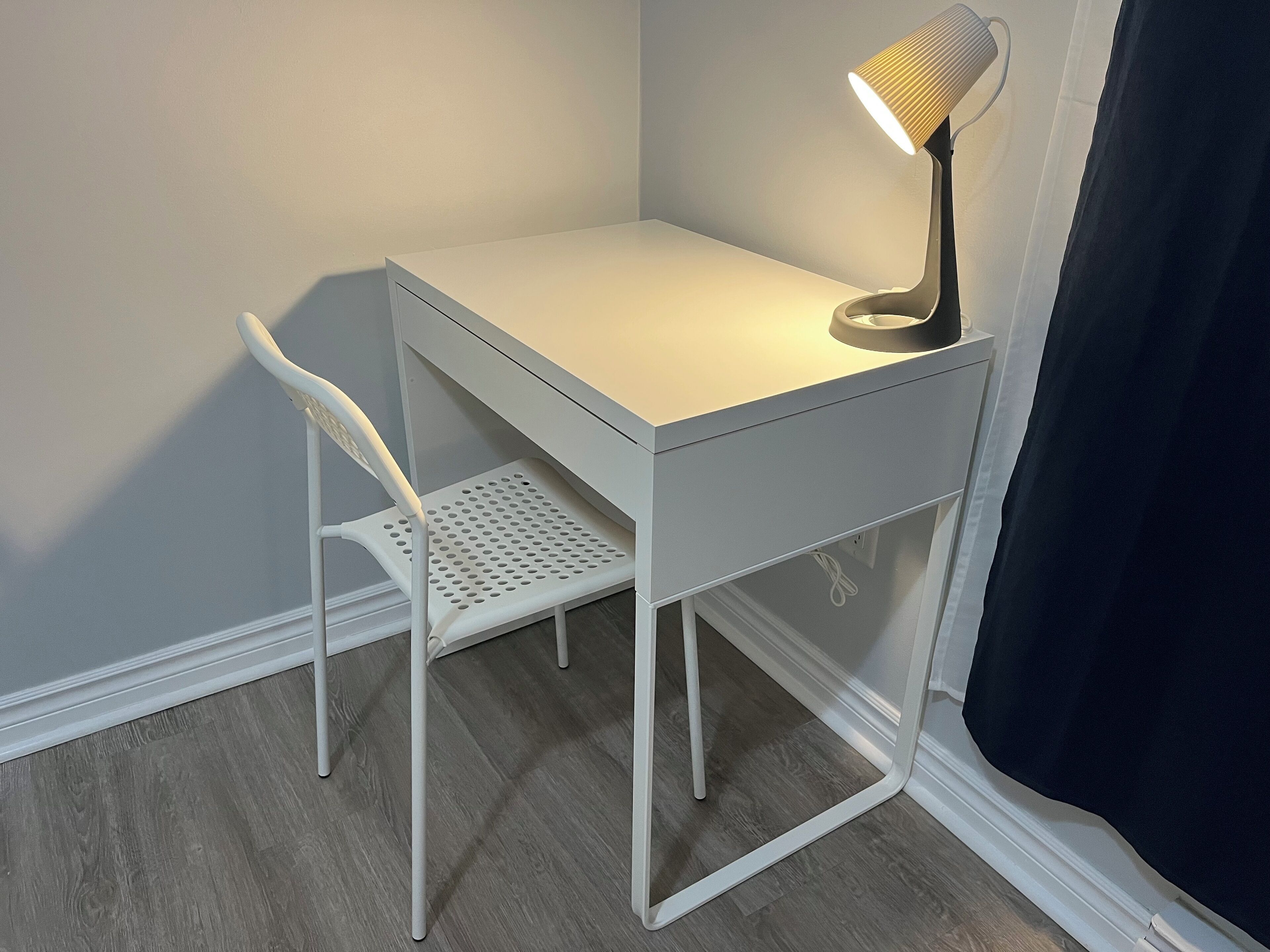 A white desk with a lamp, a white chair, and a wooden floor.
