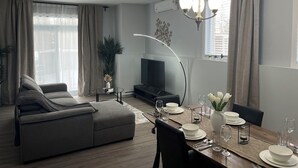 Una sala de estar moderna con un sofá, una mesa de comedor preparada para cuatro personas y un televisor de pantalla plana.
