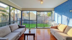 Un amplio salón con un gran ventanal corredera que da a un patio, suelo de madera y dos sofás.