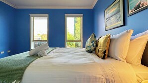 Un dormitorio con una cama grande, dos ventanas y vistas a la vegetación.