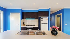Una cocina moderna con paredes azules, encimeras blancas, gabinetes oscuros, un fregadero de acero inoxidable, una estufa a gas, un refrigerador blanco y un jarrón con flores rosadas.