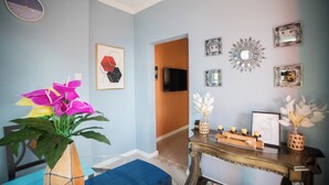 Een kamer met een blauwe muur, een klok, een lijst met kunstwerk en een console tafel met kaarsen.