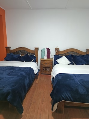 A double room with two beds, each with dark blue bedding and white pillows. There is a wooden nightstand between the beds with a telephone and a small drawer. The room has wooden flooring and white walls. - Hotel The Swit Real Centro (Tunja)