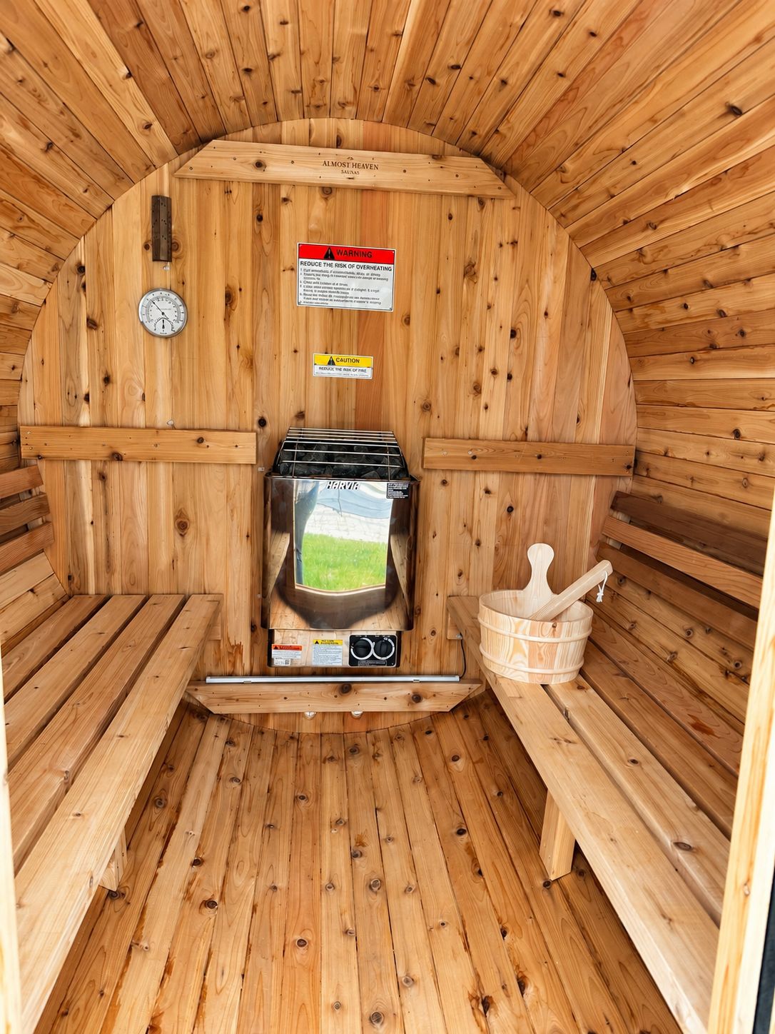 A sauna with wooden walls, a control panel, a bench, and a bucket.