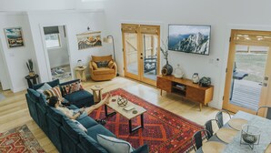 Un salon moderne avec un canapé bleu, une table basse en bois et un tapis rouge. On y trouve un meuble en bois orné d’objets décoratifs et un téléviseur fixé au mur.