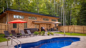 Une maison en bois avec une piscine, un espace salon extérieur et une clôture en bois.