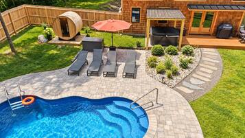 Une piscine avec une terrasse en bois, des chaises longues et un jacuzzi.