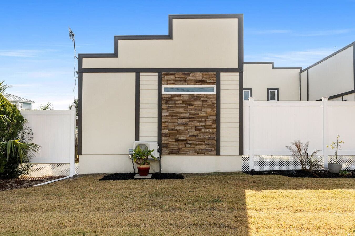 A modern house with a stone accent wall, a white fence, and a small garden with potted plants.