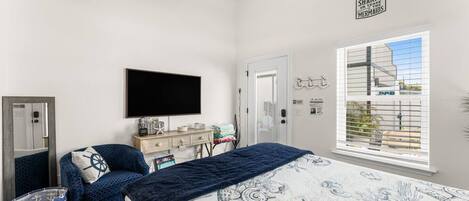 Un dormitorio con cama, escritorio, televisión, ventana y una vista, además de un cartel en la pared.
