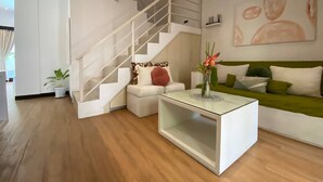 Ein modernes Wohnzimmer mit Treppe, einem weißen Sofa, einem Glastisch und einem grünen Sofa.
