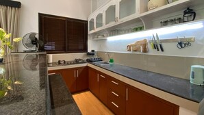 Eine moderne Küche mit einer Granitabdeckung, Holzschränken und einem eingebauten Backofen. Ein Fenster mit Jalousien, ein Ventilator und ein Regal mit Küchenutensilien sind ebenfalls vorhanden.
