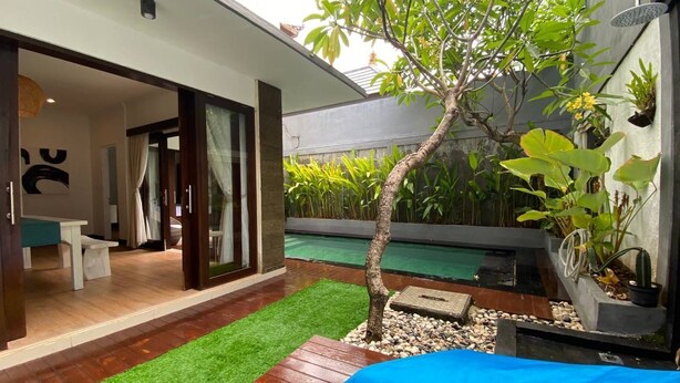 Eine moderne Terrassenanlage im Freien mit Pool, einem kleinen Baum und einer Sitzgruppe mit blauen Kissen.