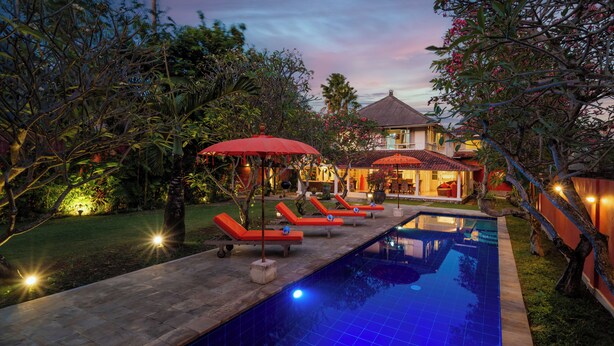 A pool area with lounge chairs and umbrellas, surrounded by greenery and a house in the background. - Seminyak Villa Kubuku 4 bedrooms (Bali)