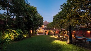 A well-maintained garden with a pool, a house with a red roof, and a lawn. - Seminyak Villa Kubuku 4 bedrooms (Bali)