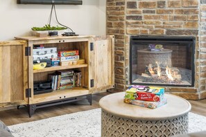 A cozy living room with a wooden cabinet, a fireplace, and a round table with a game box.