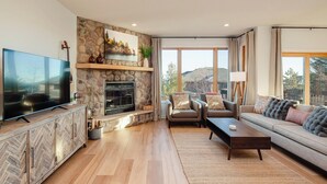 Ein modernes Wohnzimmer mit Kamin aus Stein, einem großen Flachbildfernseher und einer Couch mit dekorativen Kissen.