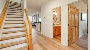 Eine Treppe mit Holzstufen und Geländer führt zu einem Raum mit Holzboden, einer Küchenzeile und einem Badezimmer mit Holztür und Spiegel.